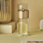 Clear Tea Infuser Portable Bottle with gold cap on a beige surface