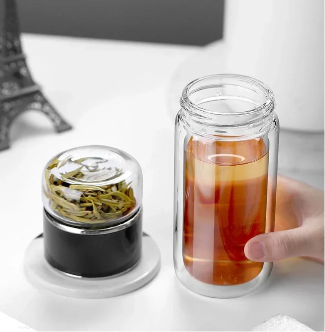 Tea Infuser Portable Bottle with tea leaves and a glass of iced tea on a white surface.