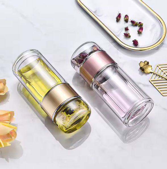 Two Tea Infuser Portable Bottle with gold and pink caps on a white surface with dried flowers.