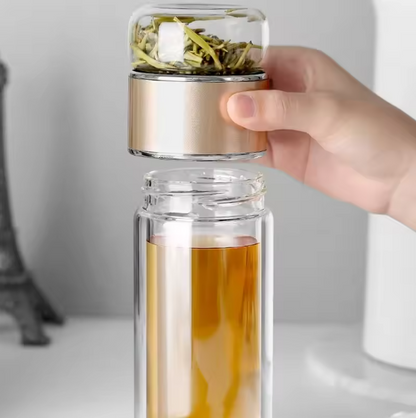 Clear glass tea infuser with gold lid held by a hand, filled with tea.